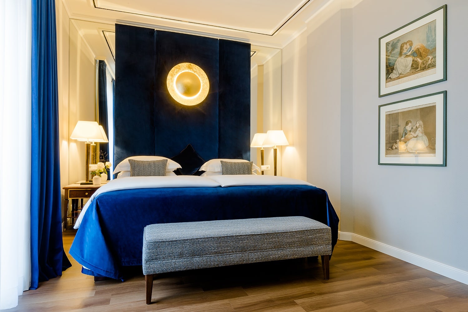 Doppelbett mit blauem Bettüberwurf steht in der Hotel Suite Köln, in der zwei Bilder an der Wand hängen